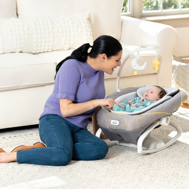 Mutter spielt mit ihrem Baby, das in der elektrischen Babyschaukel Graco All Ways Soother entspannt