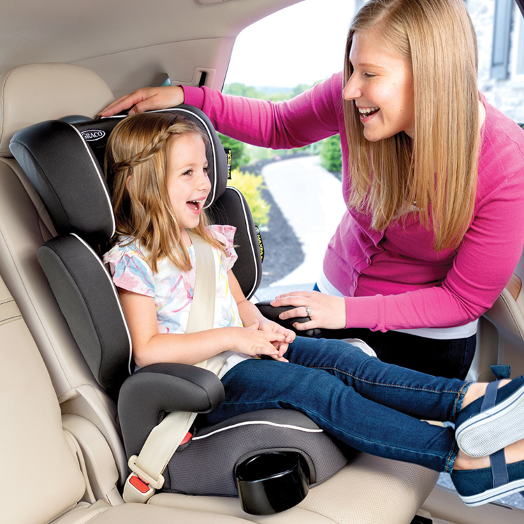 Mamma che sorride e regola il poggiatesta per la bambina seduta nel seggiolino auto Graco Assure