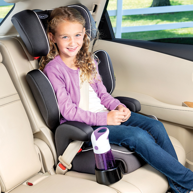 Bambina sorridente e seduta nel seggiolino auto Graco Assure con una bottiglia d'acqua nel portabicchieri