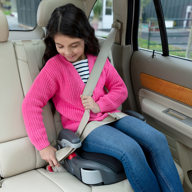 Young girl using Graco's Booster basic car seat and buckling herself in. 