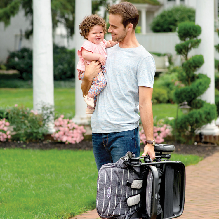 Papà che spinge Graco Breaze Lite 2 con una mano mentre tiene il bambino nell'altra