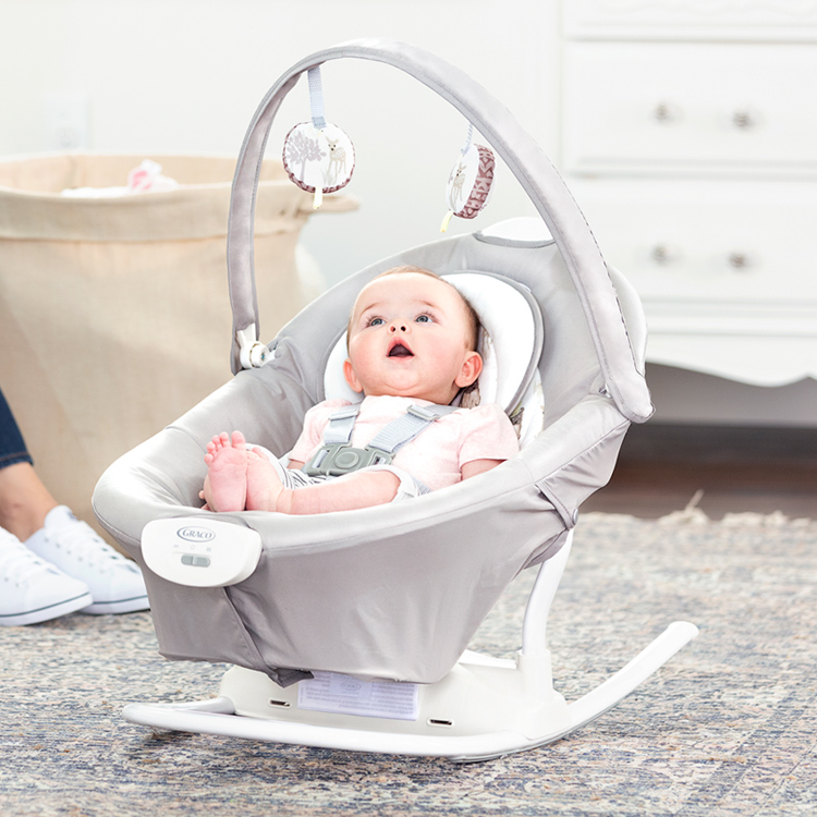 Un petit bébé regarde la barre de jouets tout en se relaxant dans la berceuse amovible du Graco Duet Sway 