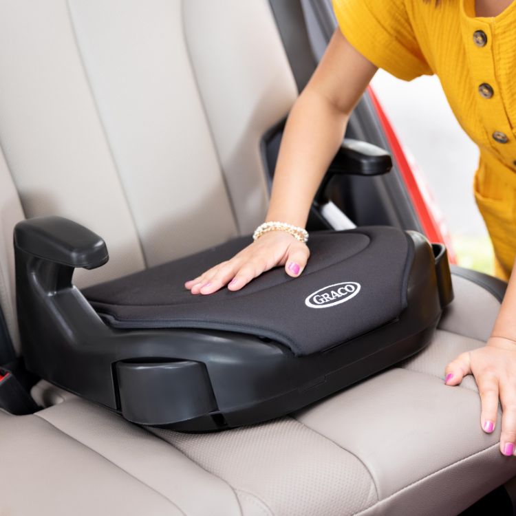 Girl putting her hand on the padded seat of Graco's Booster Basic R129 car seat.