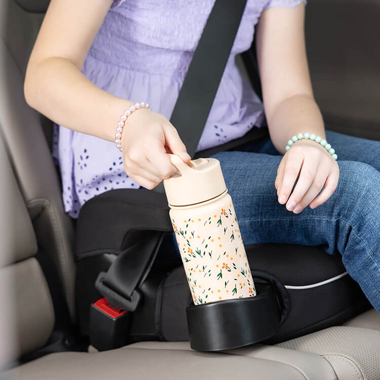 Young girl placing a water bottle in the cupholder of Graco Booster Deluxe R129 backless booster car seat. 
