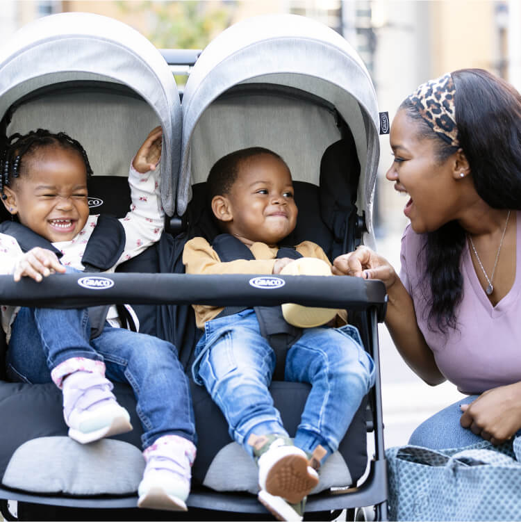 Mum interacting with smiling babies in Graco DuoRider double stroller
