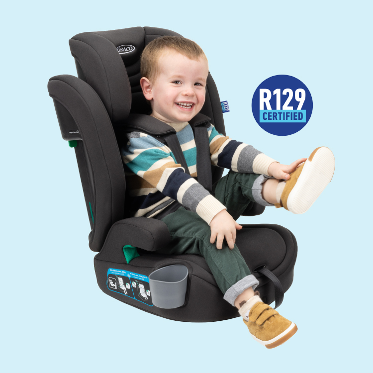 Little boy buckled in Graco Eldura R129 harness booster while laughing and kicking his feet with R129 certified logo