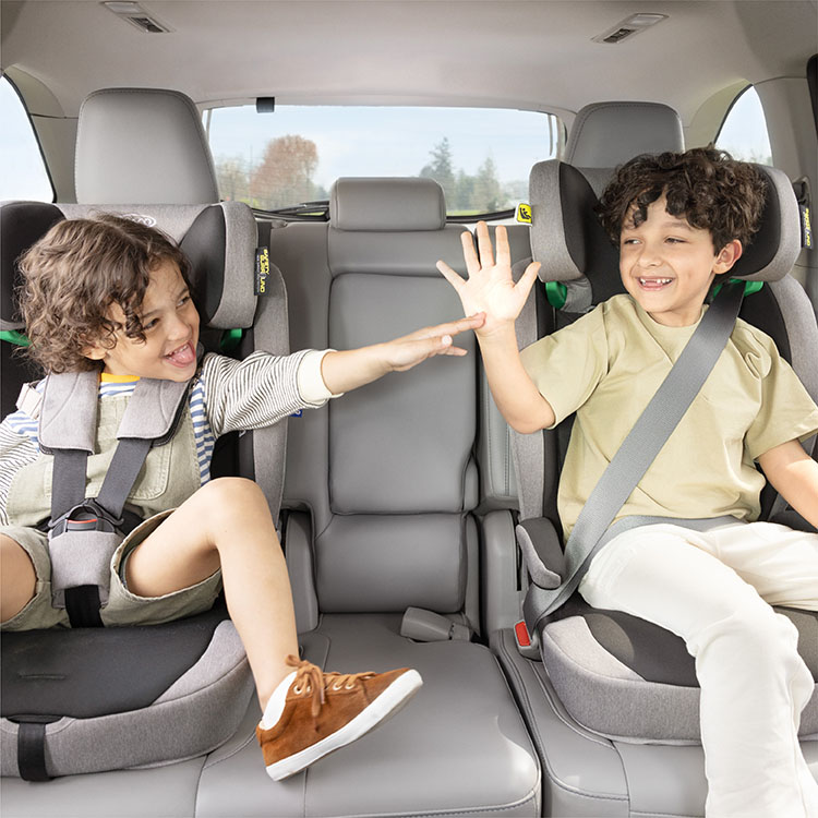 Two young boys high-fiving and buckled in to Energi i-Size R129 in highback booster mode and harness booster mode