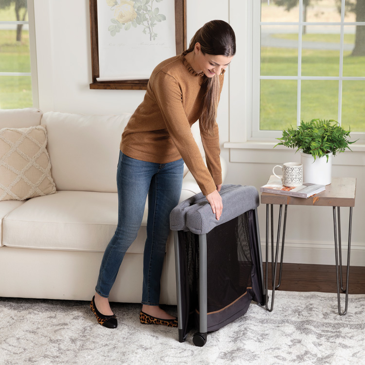 Mère repliant le lit de voyage Graco FoldLite LX avec berceau tressé dans son salon.
