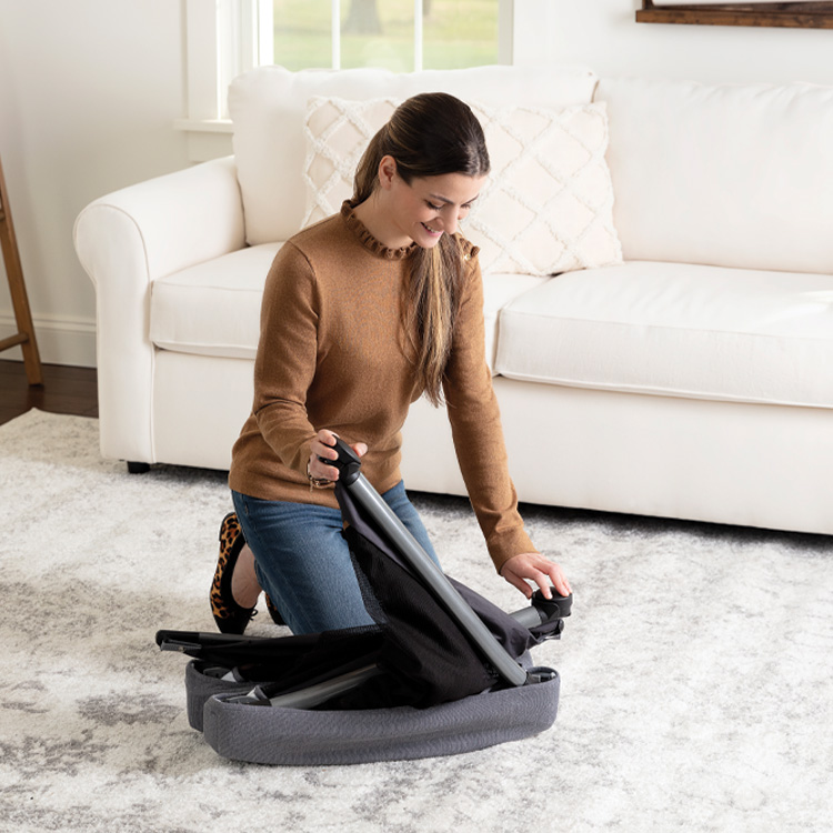 Mère repliant le lit de voyage Graco FoldLite LX avec berceau tressé pour voyage dans son salon.
