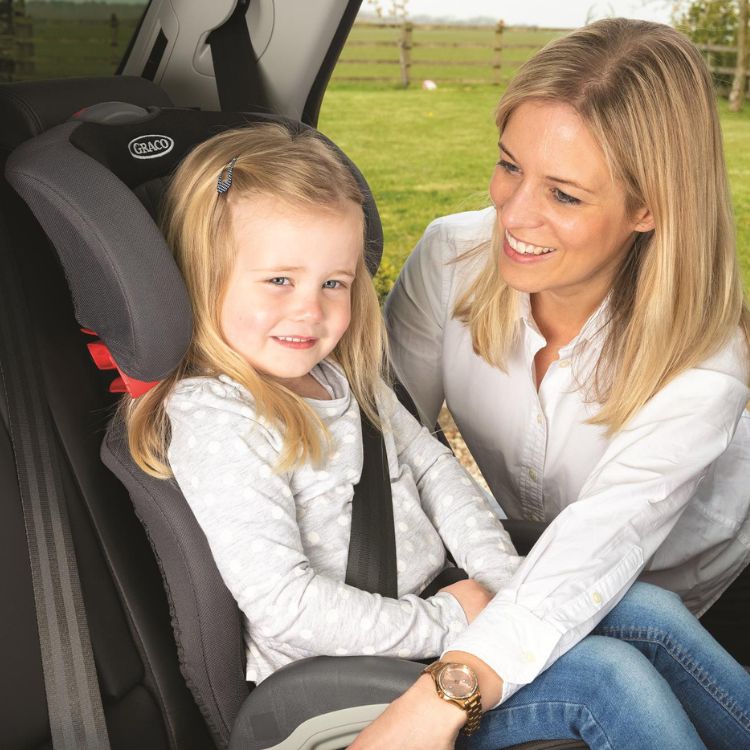 Little girl sitting in Graco Junior Maxi R44 highback booster as her mum buckles her in. 