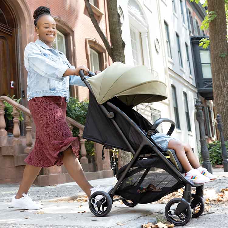 Mum walking with baby in Graco Myavo travel stroller through city.