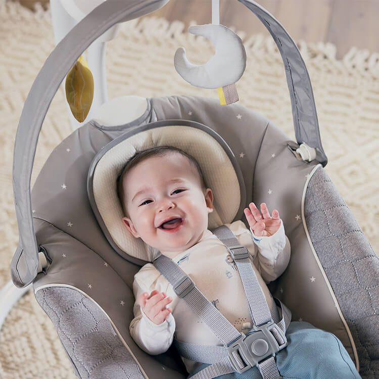 Happy baby sitting in Graco SoftSway 2-in-1 silent smart swing in living room.