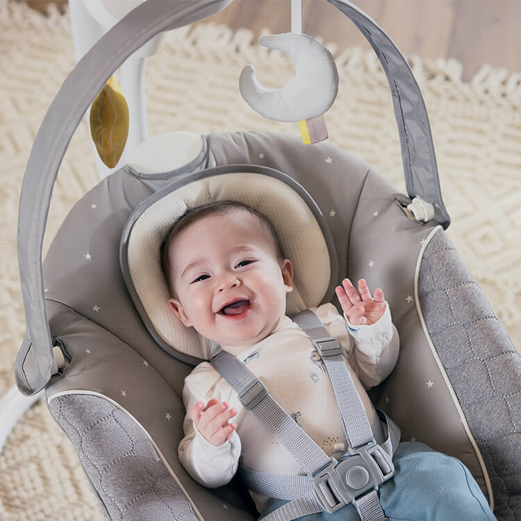 Happy baby sitting in Graco SoftSway 2-in-1 silent smart swing in living room. 