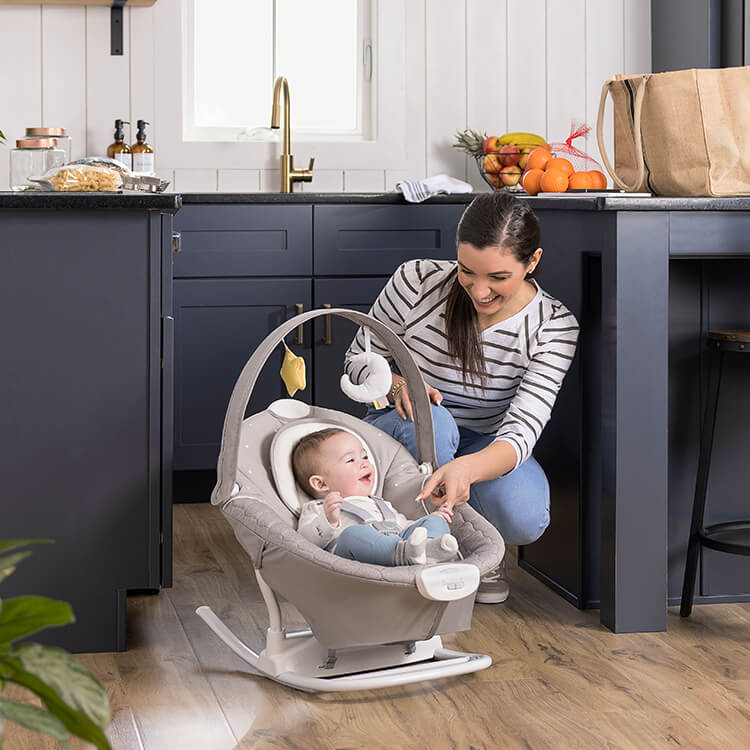 Lächelndes Baby sitzt in der Graco® SoftSway™ Wippe in der Küche.
