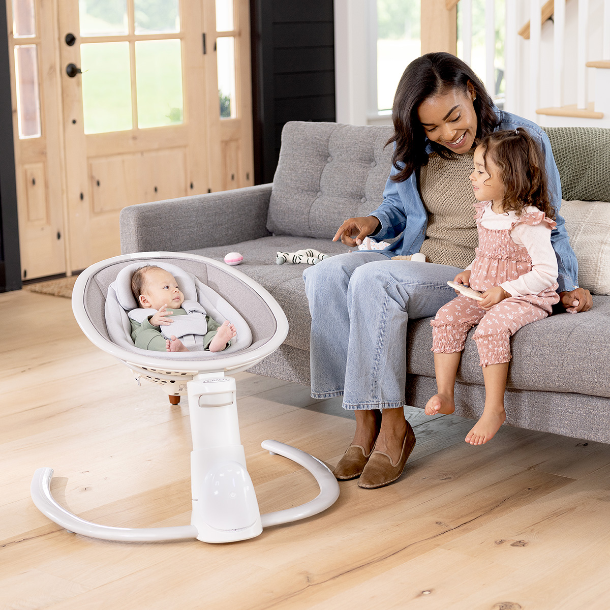 Infant swaying in Sway 'n Grow 3-in-1 silent swing while Mum and young girl are sitting on the sofa
