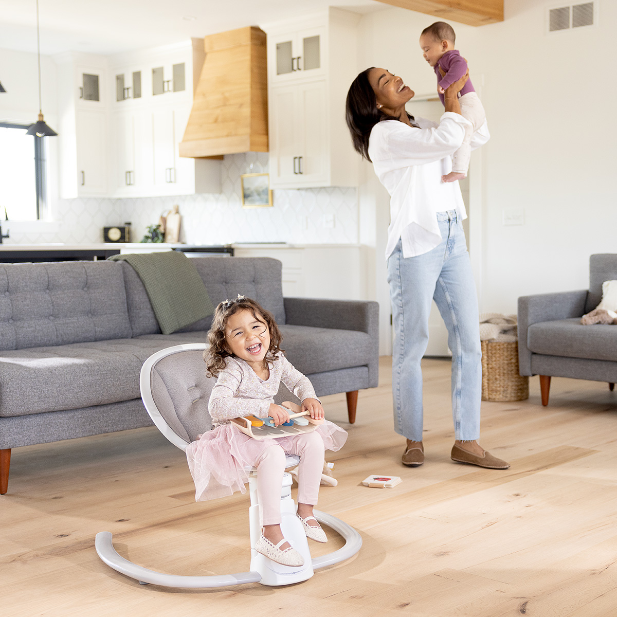 Young girl sitting in Sway 'n Grow 3-in-1 silent swing while Mum is holding baby
