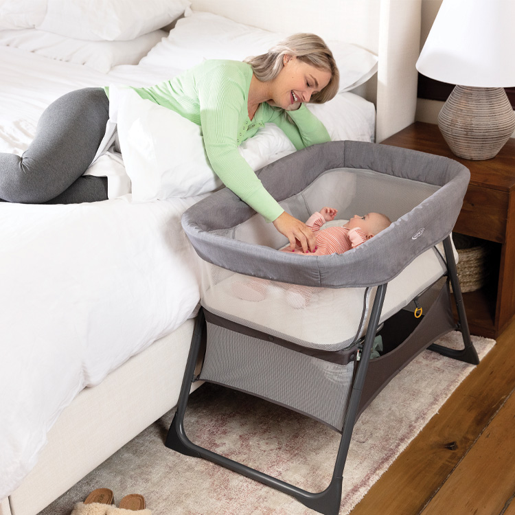 Mum lying in bed next to baby in Graco Side-By-Side Bedside Bassinet.