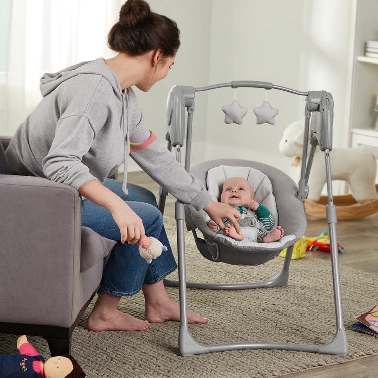Woman sitting on the couch pushing baby in Graco Slim Spaces swing