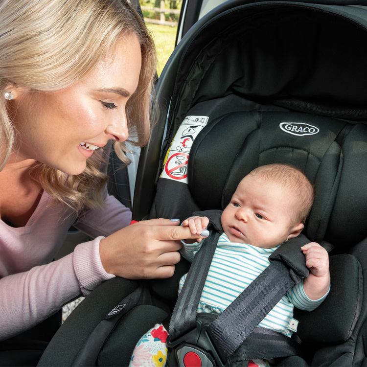 Madre abrochando a su bebé en la silla portabebés Graco SnugRide i-Size en color midnight black dentro del vehículo