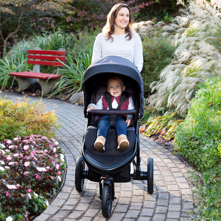 Mutter im Park schiebt ihren Sohn im Kinderwagen Graco TrailRider