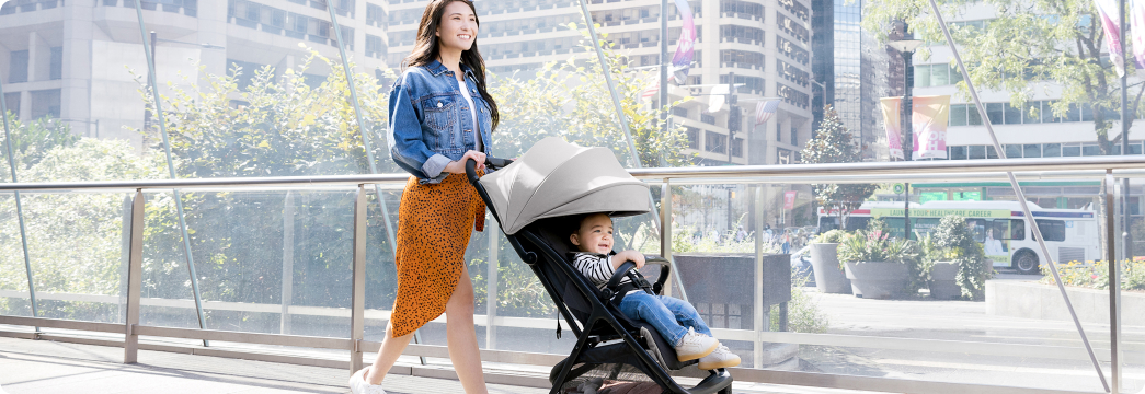 Mum smiling and walking while pushing toddler in Myavo quick-folding lightweight travel stroller.