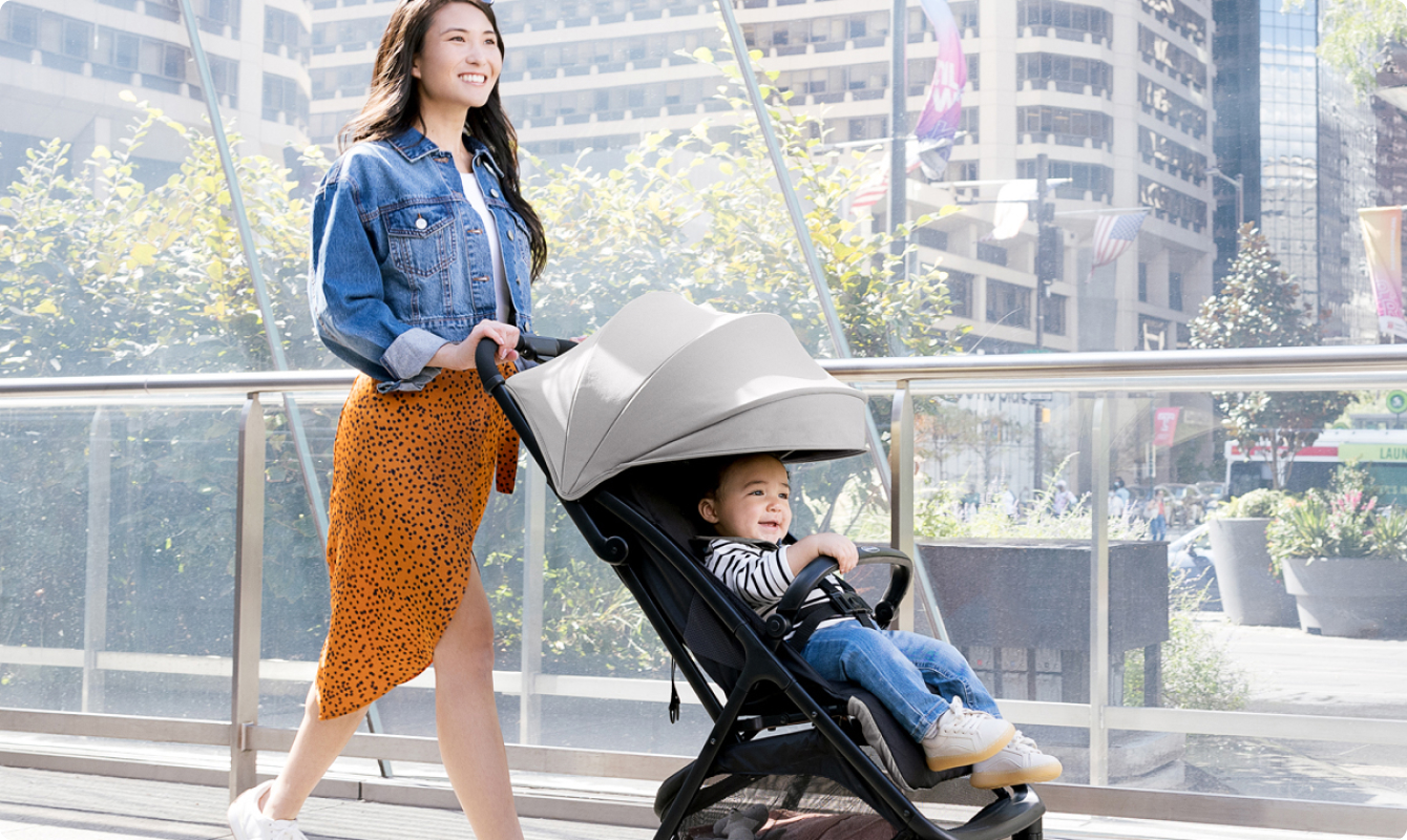 Mum smiling and walking while pushing toddler in Myavo quick-folding lightweight travel stroller.