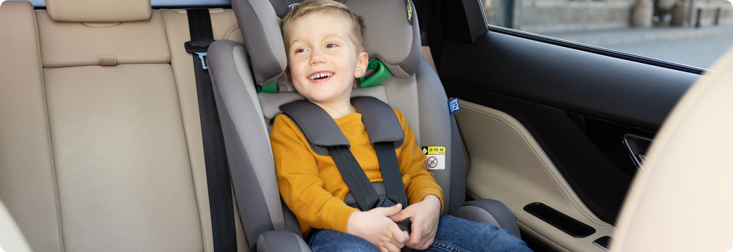 Young boy laughing while buckled into FlexiGrow R129 2-in-1 harness booster car seat.