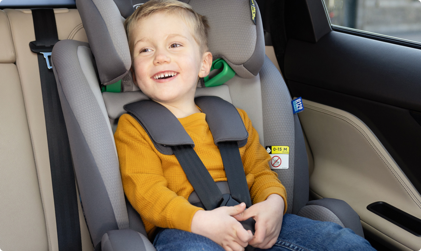 Young boy laughing while buckled into FlexiGrow R129 2-in-1 harness booster car seat.